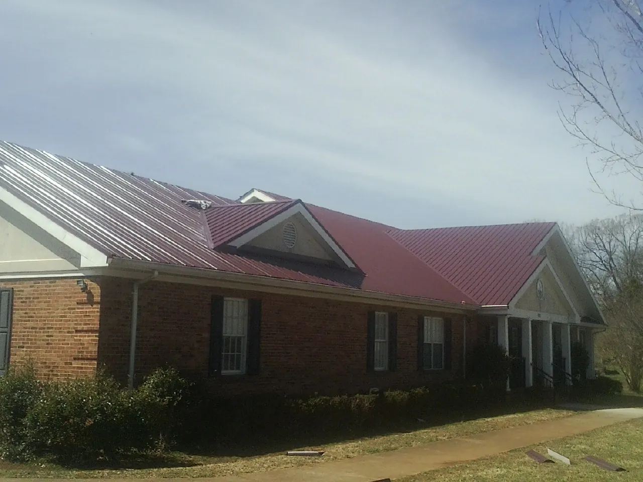 Red metal roof with gabled entries on a long brick building, from a Hail Damage Roof Repair job in Margaretville