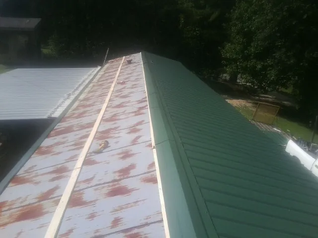 Old rusted panels beside newly installed green metal roofing — Wind Damage Roof Repair by Roofing Brothers in Margaretville