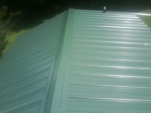 New green metal panels meeting at the ridge of a roof — Flat Roof Repair work by our crew in Margaretville