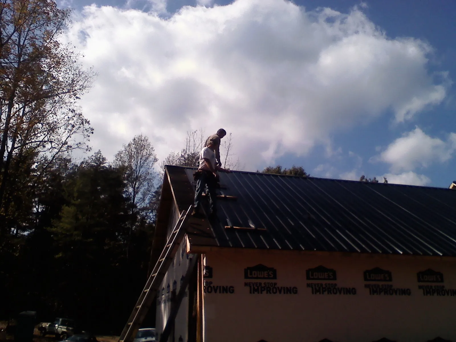 Roofer fastening dark metal panels high against a cloudy sky, from a Roof Inspection job in Margaretville
