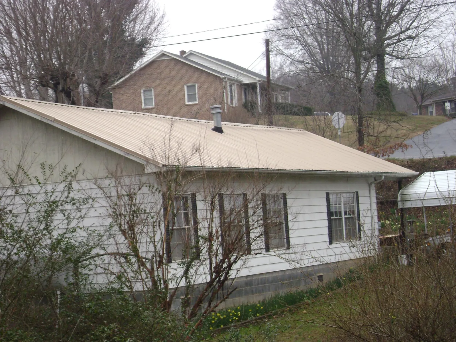 Tan metal roof on a white sided house set into a hillside — Commercial Roofing by Roofing Brothers in Margaretville